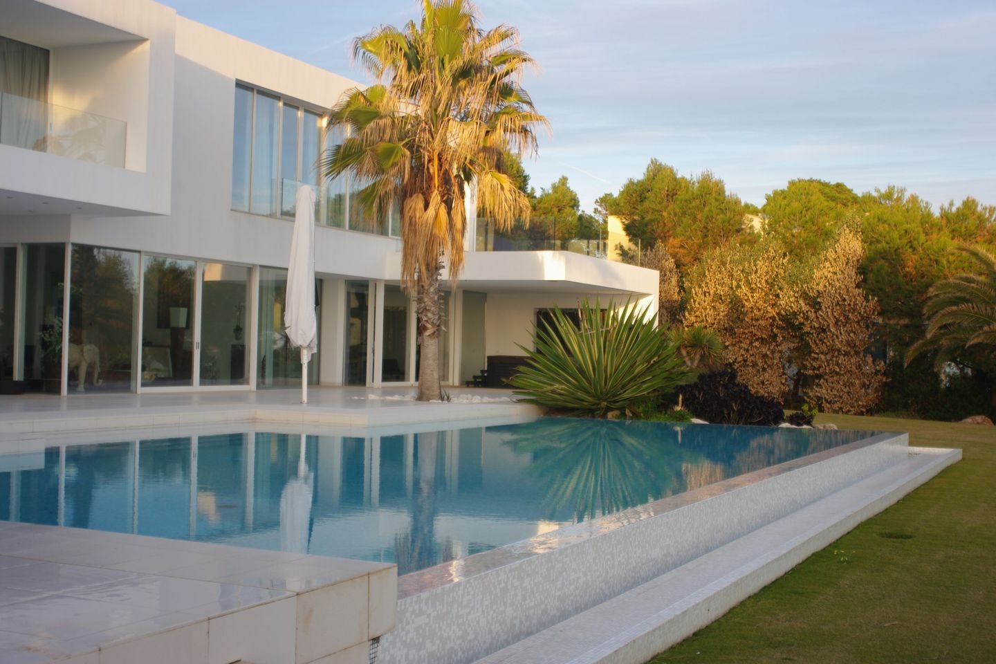 Überlaufpool vor einer modernen weißen Villa mit Palmen